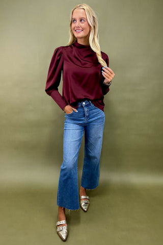 Woman wearing a burgundy top and blue jeans against a green background