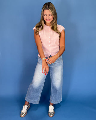 Woman wearing a pink shirt and light blue jeans against a blue background