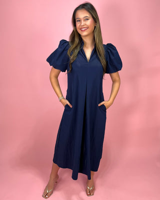 Woman wearing a navy blue dress with puff sleeves against a pink background
