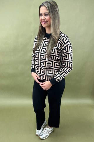 Woman wearing a black and white patterned sweater with black pants on a green background