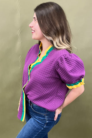 Woman wearing a purple textured top with colorful trim against a green background