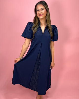 Woman wearing a navy blue dress against a pink background