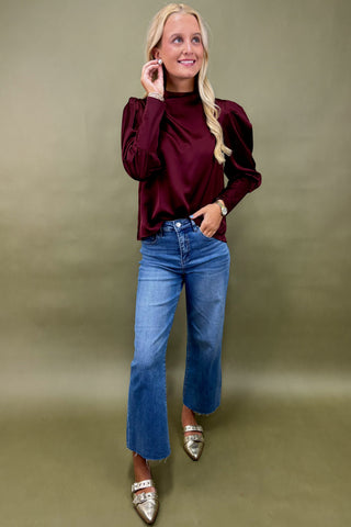 Woman wearing a burgundy top and blue jeans against a green background