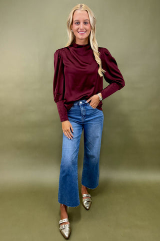 Woman wearing a burgundy top and blue jeans against a green background