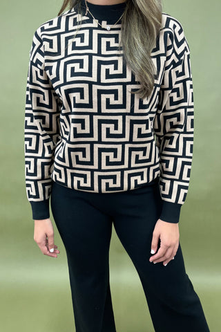 Person wearing a black and white geometric patterned sweater against a green background