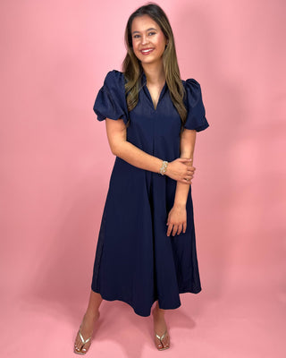 Woman wearing a navy blue dress against a pink background
