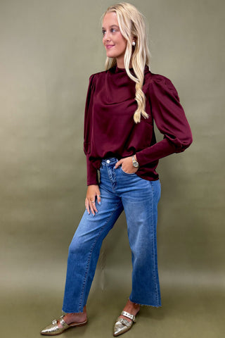 Woman wearing a burgundy blouse and blue jeans against a green background