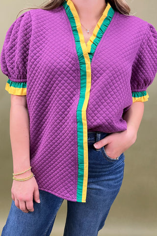 Person wearing a purple quilted jacket with colorful trim on a plain background