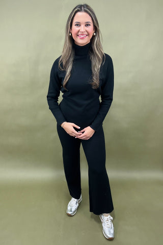 Woman wearing a black outfit with silver shoes on a beige background