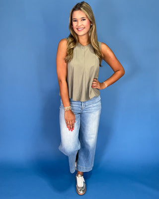 Woman wearing a sleeveless top and jeans against a blue background