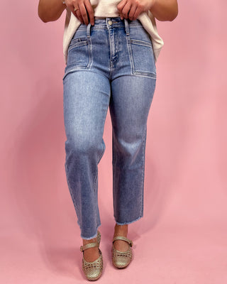 Person wearing blue jeans and gold sandals on a pink background