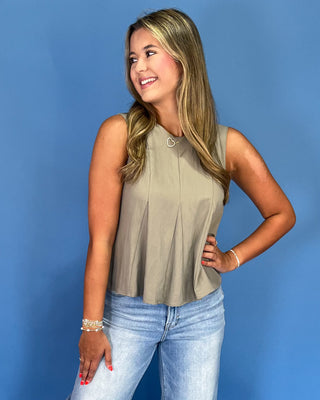 Woman wearing a beige sleeveless top and blue jeans against a blue background