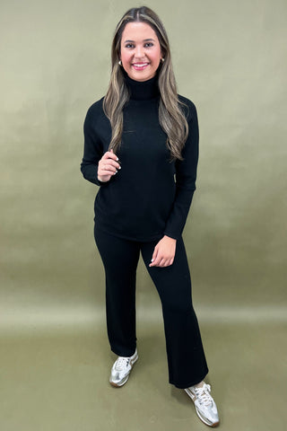 Woman wearing a black turtleneck and pants with white sneakers on a beige background