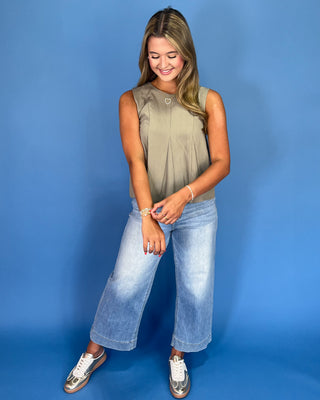 Woman wearing a sleeveless top and wide-leg jeans against a blue background
