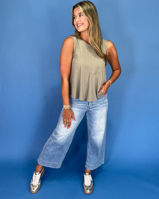 Woman wearing a sleeveless top and jeans against a blue background