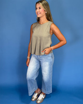 Woman wearing a sleeveless top and jeans against a blue background