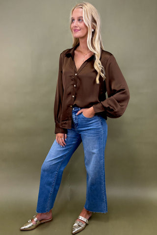 Woman wearing a brown shirt and blue jeans against a green background