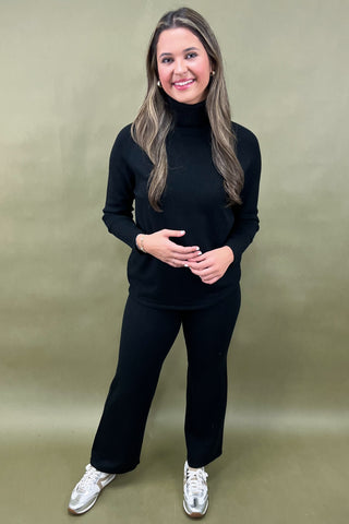 Woman wearing a black outfit with white sneakers on a beige background