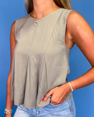 Woman wearing a sleeveless gray top and blue jeans against a blue background