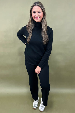 Woman wearing a black outfit with white sneakers against a beige background