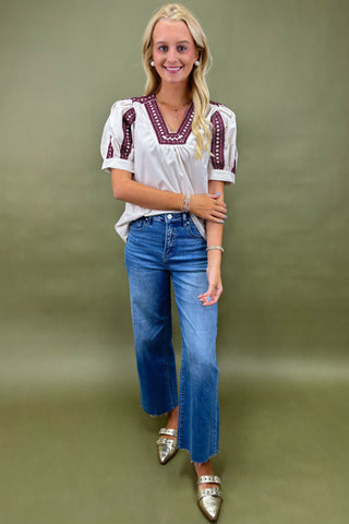 Woman wearing a white blouse with red embroidery and blue jeans on a green background