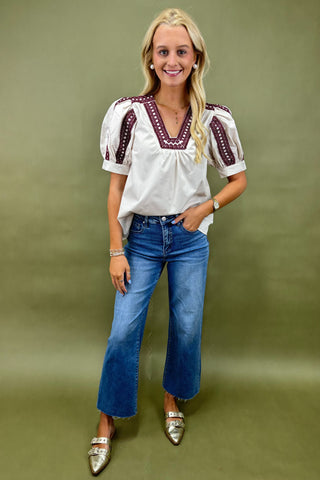 Woman wearing a white blouse with red embroidery and blue jeans on a green background