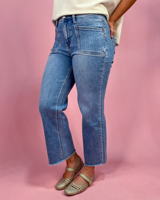 Person wearing blue jeans and gold flats on a pink background