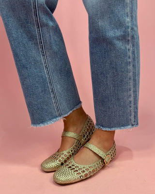 Gold open-toe shoes worn with blue jeans on a pink background