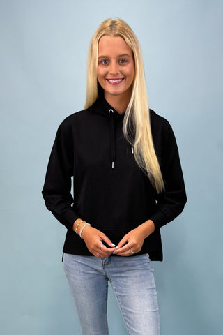 Woman wearing a black quarter-zip sweatshirt and light blue jeans against a light blue background