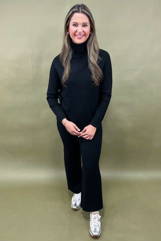 Woman wearing a black turtleneck and black pants with white sneakers on a beige background