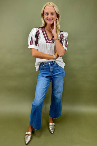 Woman wearing a white blouse with red embroidery and blue jeans on a green background