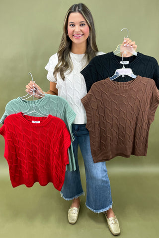 Woman holding four sweaters on hangers against a green background