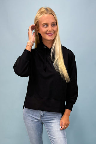Woman wearing a black shirt and light blue jeans against a light gray background