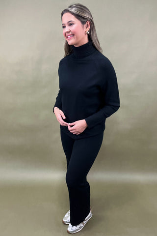 Woman wearing a black turtleneck and pants against a beige background