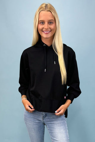 Woman wearing a black hoodie and light blue jeans against a light blue background