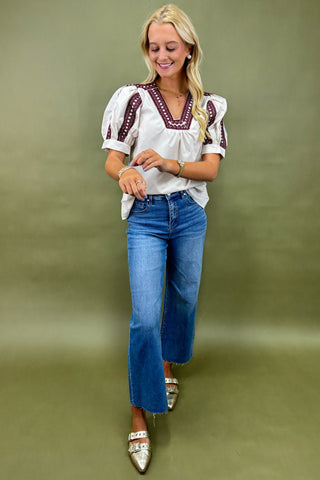 Woman wearing a white blouse with red embroidery and blue jeans on a green background