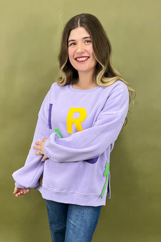 Woman wearing a light purple sweatshirt with a large yellow 'R' on a green background