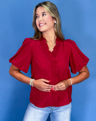 Woman wearing a red blouse with ruffled sleeves against a blue background