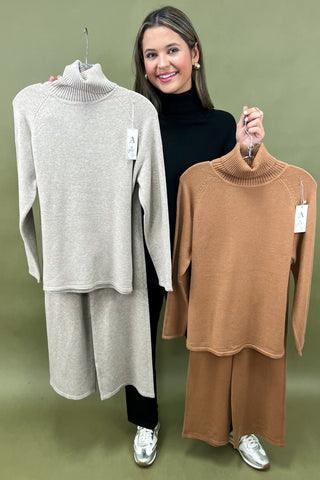 Woman holding two hangers with turtleneck sweaters against a green background