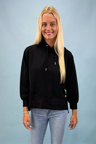 Woman wearing a black hoodie and light blue jeans against a gray background