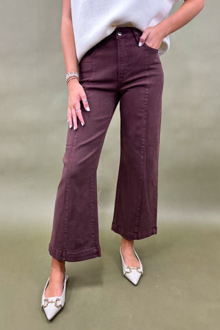 Person wearing maroon pants and white shoes on a plain background