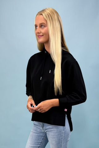 Woman wearing a black jacket and light blue jeans against a light blue background