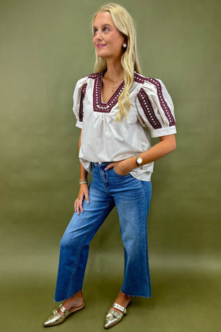 Woman wearing a white blouse with red embroidery and blue jeans on a green background