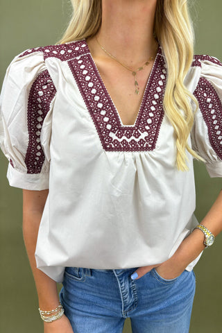 White blouse with red embroidery worn by a person, with a neutral background