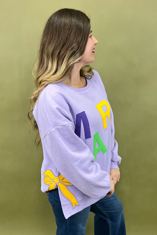 Woman wearing a light purple sweatshirt with colorful letters and bows on a green background