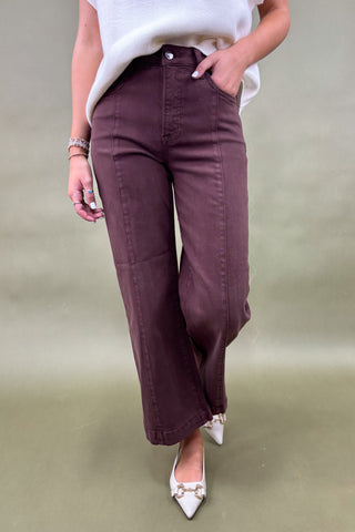 Person wearing brown wide-leg pants and white shoes on a plain background