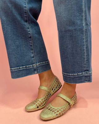 Gold open-toe shoes worn with blue jeans on a pink background