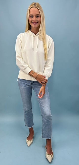 Woman wearing a white hoodie and blue jeans against a light blue background