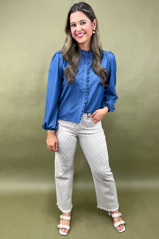 Woman wearing a blue blouse and white jeans against a green background