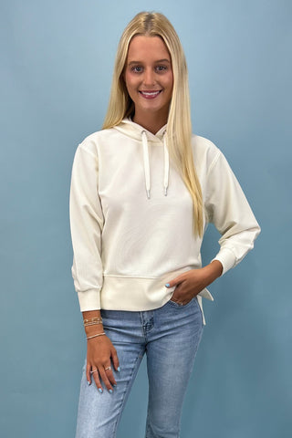 Woman wearing a cream hoodie and blue jeans against a light blue background